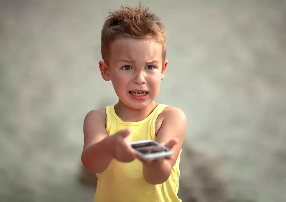 enfant tenant un smartphone en le repoussant et ayant le visage triste et en colére de quelque chose qu'il a vu sur le téléphone bloomapp éducation social media pour enfants apprentissage apprendre